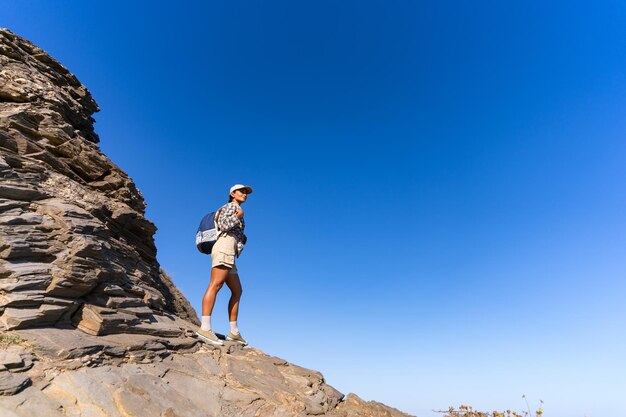 Foto una chica turista con una mochila en la espalda en el verano se encuentra en la cima de una montaña