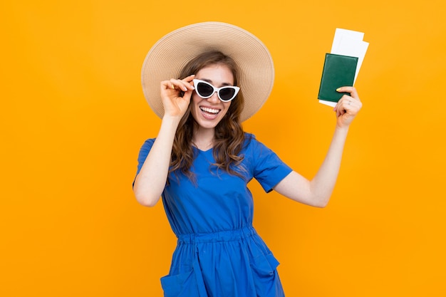 Chica turista con pasaporte y boletos en el fondo de una pared naranja sonriendo