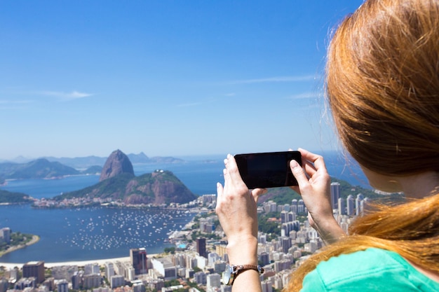 Chica turista toma una foto del paisaje de Río con un teléfono inteligente
