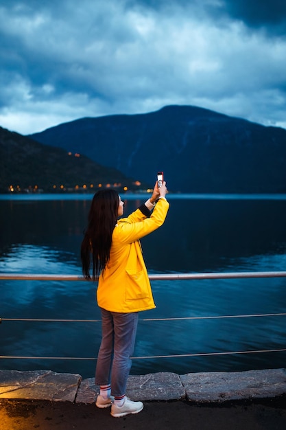 La chica turista toma una foto por teléfono junto al lago en Noruega Mujer activa relajante