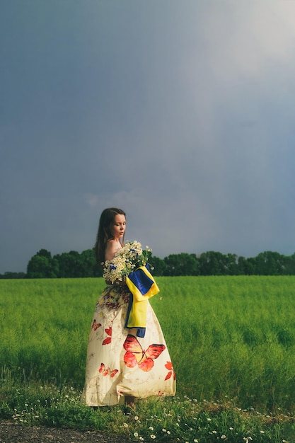 Chica ucraniana con una bandera azulamarilla en sus manos en el fondo del campo