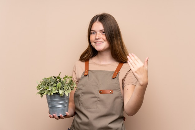 Chica ucraniana jardinero adolescente sosteniendo una planta invitando a venir