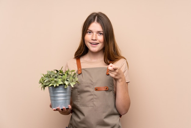 Chica ucraniana jardinero adolescente sosteniendo una planta te señala con el dedo