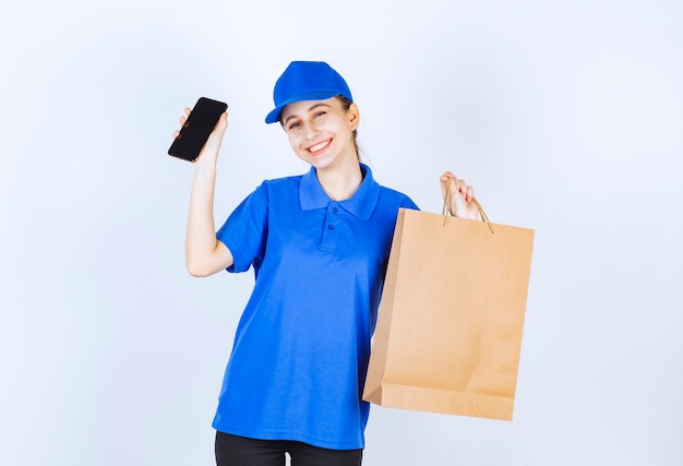 Chica en uniforme azul sosteniendo una bolsa de cartón y un teléfono inteligente negro.