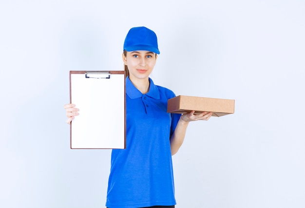 Foto chica en uniforme azul sosteniendo una caja de cartón para llevar y una lista de clientes.