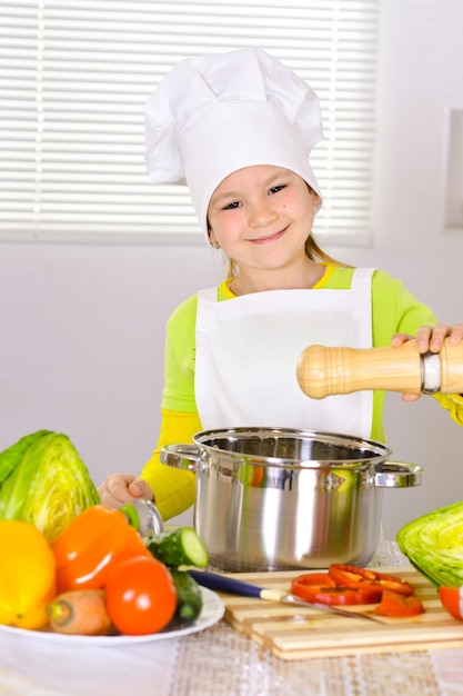 Chica con uniforme de chef cocinando en la cocina agregando sal al plato