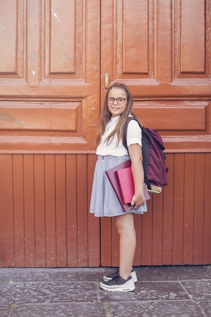 Foto chica en uniforme escolar con mochila antes de puertas grandes