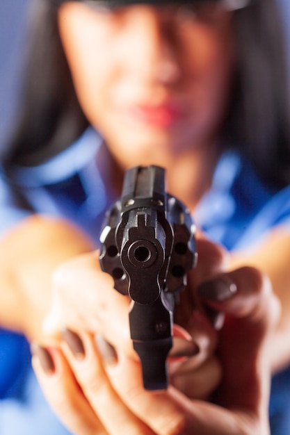 Una chica en uniforme con una pistola posa en el estudio. El énfasis está en la pistola que está en primer plano.