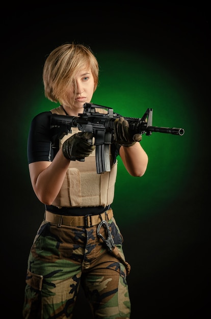 La chica de uniforme con una pistola posando, apuntando, recargando, disparando, sobre un fondo oscuro en el estudio