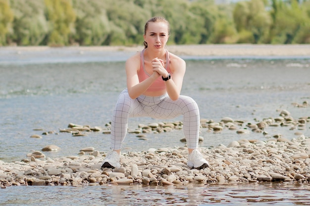 Chica en uniformes deportivos se estira en la orilla del río