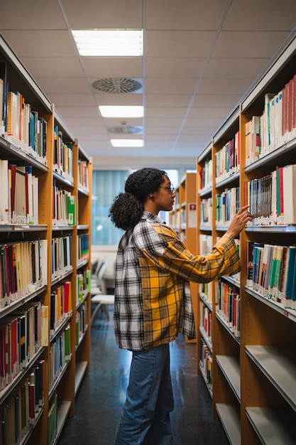 Una chica de la universidad eligiendo un libro para leer para un examen está en una biblioteca