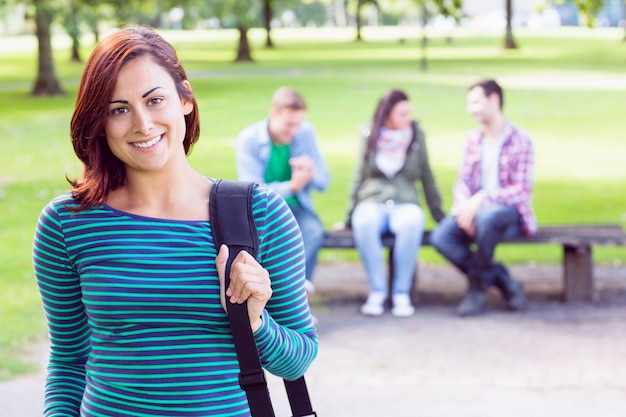 Chica universitaria sonriendo con estudiantes borrosas en el parque