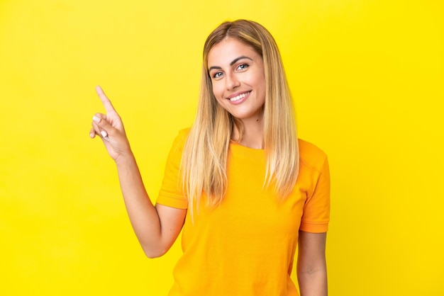 Chica uruguaya rubia aislada de fondo amarillo mostrando y levantando un dedo en señal de lo mejor