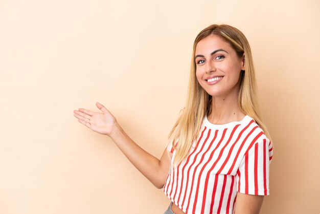 Chica uruguaya rubia aislada de fondo beige extendiendo las manos a un lado para invitar a venir