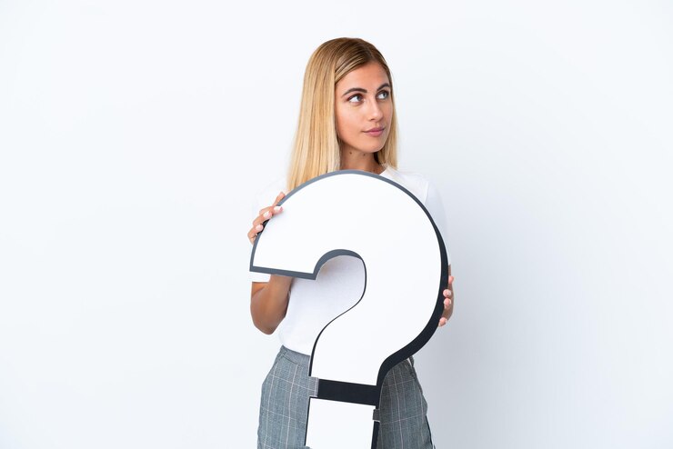 Foto chica uruguaya rubia aislada de fondo blanco sosteniendo un icono de signo de interrogación y mirando hacia el lado