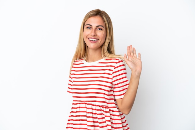 Chica uruguaya rubia aislada sobre fondo blanco saludando con la mano con expresión feliz