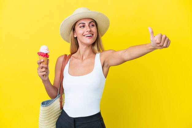 Chica uruguaya rubia en verano sosteniendo helado aislado en fondo amarillo dando un gesto de aprobación