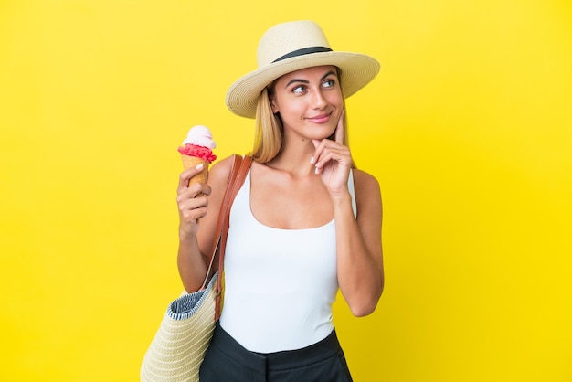 Chica uruguaya rubia en verano sosteniendo helado aislado en un fondo amarillo pensando en una idea mientras mira hacia arriba