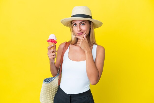 Chica uruguaya rubia en verano sosteniendo helado aislado en el pensamiento de fondo amarillo