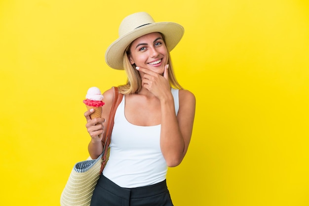 Chica uruguaya rubia en verano sosteniendo helado aislado sobre fondo amarillo feliz y sonriente