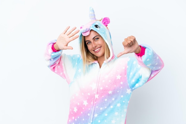 Chica uruguaya rubia vistiendo un pijama de unicornio aislado sobre fondo blanco contando seis con los dedos