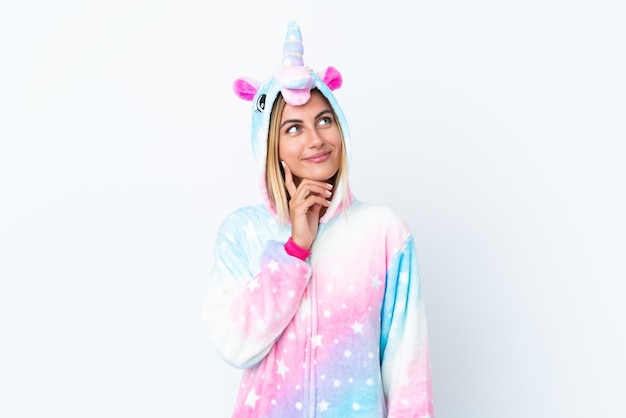 Chica uruguaya rubia vistiendo un pijama de unicornio aislado sobre fondo blanco pensando en una idea mientras mira hacia arriba