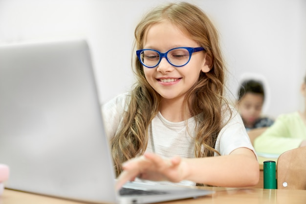 Chica usando computadora moderna durante la lección en la escuela