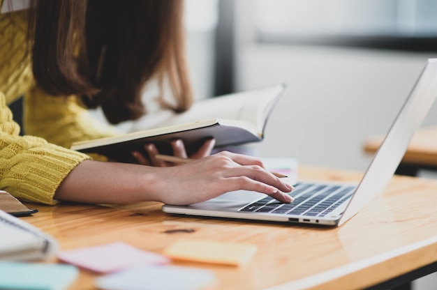 Foto chica usando una computadora portátil y sosteniendo un libro en la mano, buscó información para aprender, aprendizaje en línea, búsqueda de información en internet.