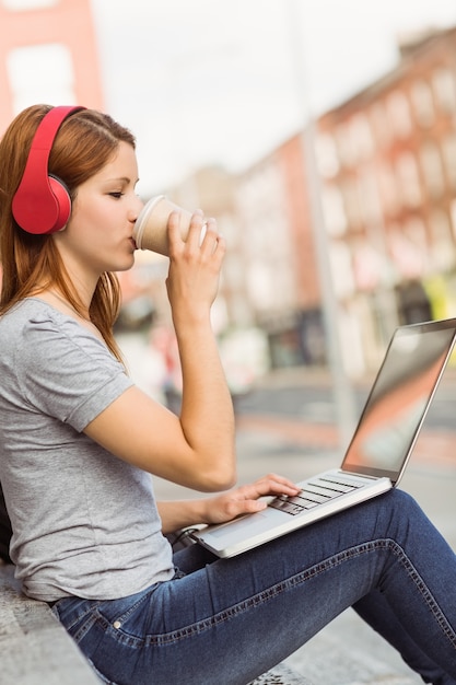 Chica usando laptop, escuchando música y tomando café