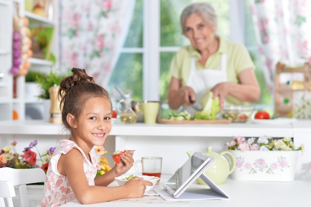 Chica usando tableta con mujer cocinando en el fondo