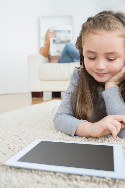 Chica usando tableta con su madre leyendo el periódico en el sofá