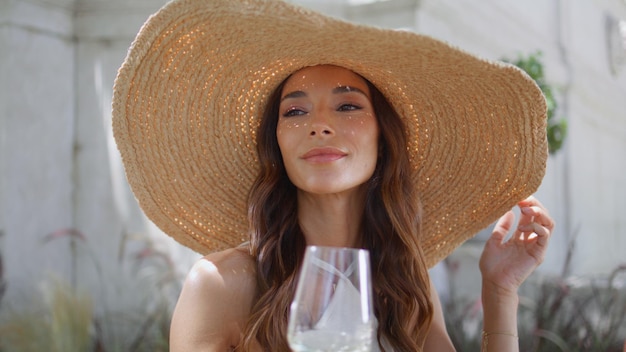 Chica de vacaciones bebiendo un vaso de vino en un café soleado primer plano sombrero de paja mujer descansar