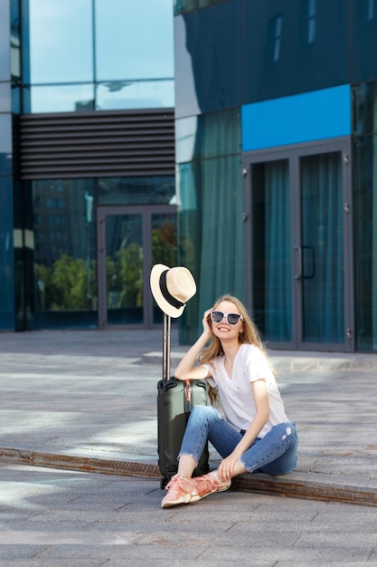 Chica de vacaciones con gafas con equipaje se sienta en el aeropuerto