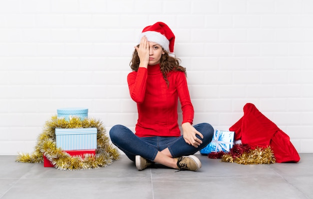 Chica en vacaciones de navidad sentada en el suelo cubriendo un ojo con la mano