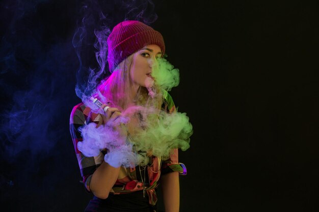 Chica vaping. Joven inconformista mujer vape e-cig sobre fondo negro. Estilo hip-hop. Concepto de vapor. Vapear cigarrillos electrónicos. Tiro del estudio