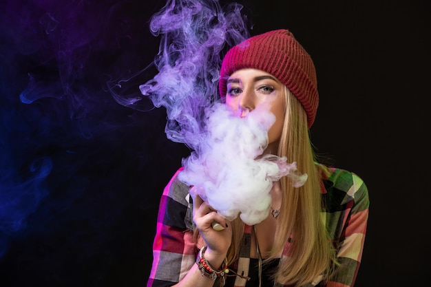 Chica vaping. Mujer joven inconformista vape e-cig en estudio sobre fondo negro. Estilo hip-hop. De cerca.