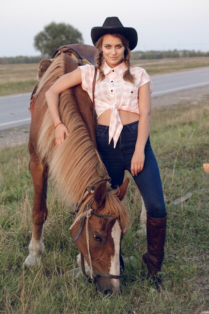 Foto chica en vaqueros vaqueros de camisa de sombrero negro de vaquero con caballo