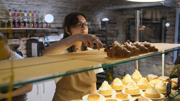 La chica vendedora pone croissants a la venta en la ventana de la panadería.