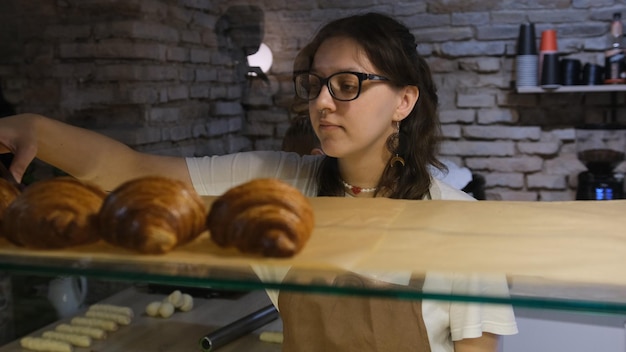 La chica vendedora pone croissants a la venta en la ventana de la panadería.