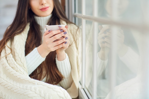 Chica en la ventana con una taza de café en invierno.