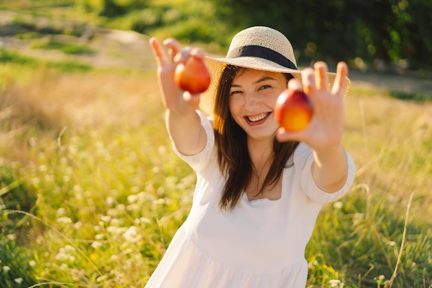 Chica de verano feliz y despreocupada en el campo al aire libre con fruta de melocotón naranja Mujer joven come melocotón Ajuste de picnic de verano