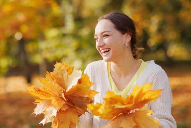 Chica vestida de amarillo en el parque de otoño se regocija en otoño sosteniendo hojas amarillas en sus manos cálidas