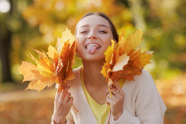 Chica vestida de amarillo en el parque de otoño se regocija en otoño sosteniendo hojas amarillas en sus manos cálidas