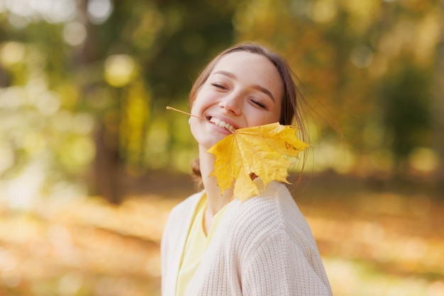 una chica vestida de amarillo en un parque de otoño se regocija en otoño sosteniendo hojas amarillas en sus manos