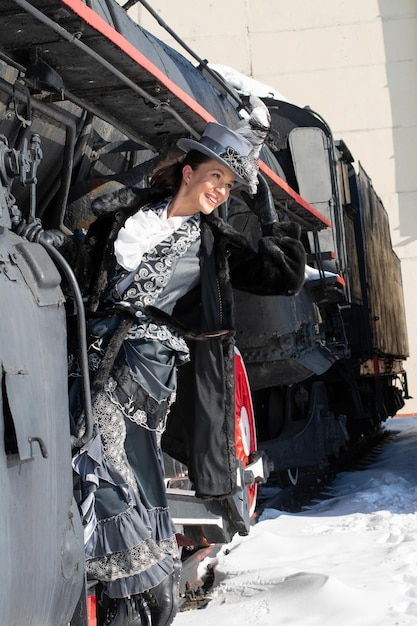 Chica vestida como una mujer noble del siglo XIX cerca de una locomotora de vapor invierno ruso