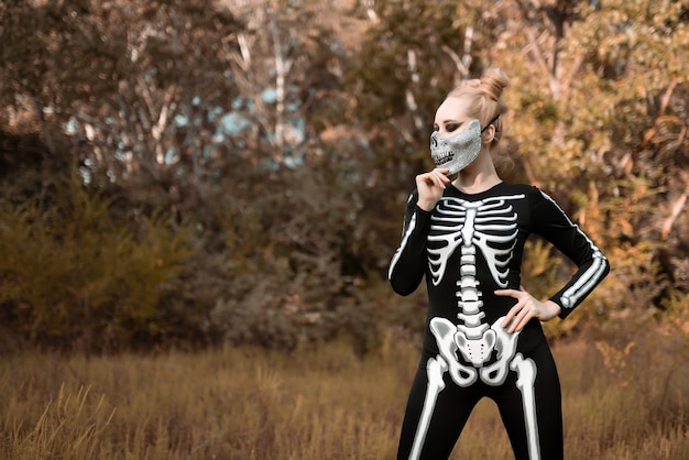Foto chica vestida de esqueleto en el bosque de otoño. se quedó de pie terriblemente, mirando a la cámara. víspera de todos los santos