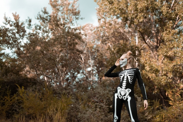 Chica vestida de esqueleto en el bosque de otoño. Se quedó de pie terriblemente, mirando a la cámara. Víspera de Todos los Santos