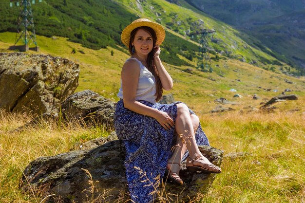 La chica vestida se sienta en una roca sosteniendo un sombrero de paja