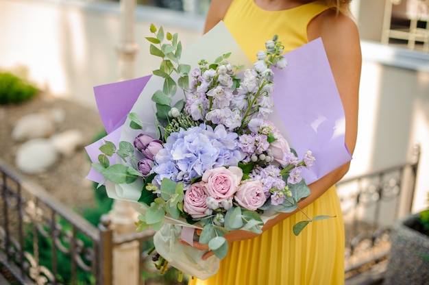 Chica vestida con un vestido amarillo con un ramo de flores de color púrpura