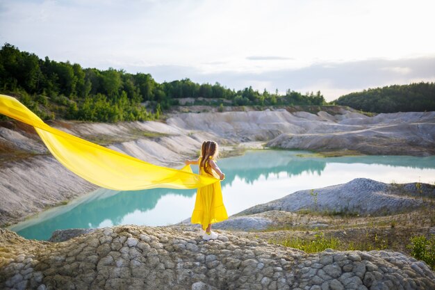 Chica con un vestido amarillo con alas en un paño amarillo cerca del lago